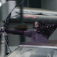 Hailee Steinfeld's Kate fires an arrow while sitting in the window of a moving car.